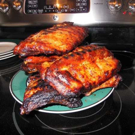Two racks of golden BBQ ribs fresh from a Forno Nardona Oven and sitting on a green plate.