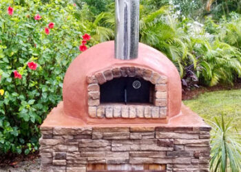 Forno Nardona Rustico Oven with terracotta colored stucco finish on a custom built base with black oven door and wooden base door.