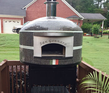 An outdoor pizza oven finished with black and white glass tiles and a custom engraved plate