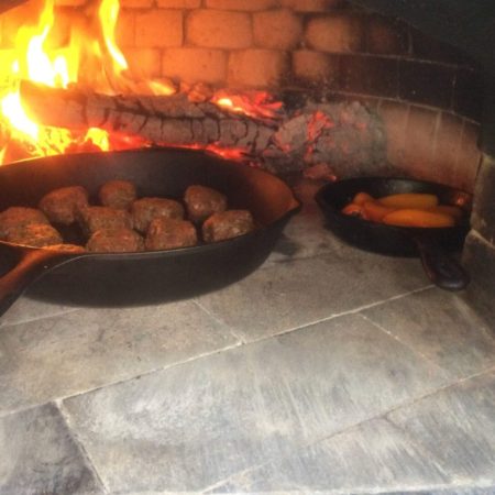 Two cast iron pans with food cooking inside a Forno Nardona brick oven.
