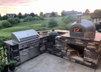 The Nardona Rustico is one of four models of Forno Nardona residential pizza ovens on a stoned base with granite countertop and a grand back yard view.