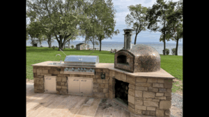 Tampa built outdoor kitchen complete with Lion Grill, Lion accessories and a Forno Nardona Rustico oven with copper tile and a beautiful backdrop of the ocean just beyond the green grass. and trees.