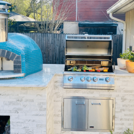 An outdoor kitchen built by Forno Nardona featuring the Nardona Rustico oven in Hawaii blue glass tile on a white countertop with Lion grill.