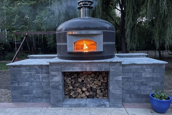 Forno Nardona Napoli oven on customer built stone finished base with wood storage underneath and flame inside the oven dome.
