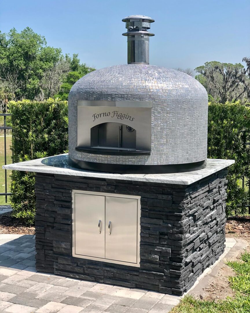 32" Nardona Napoli oven in moon tile set on a white granite surface on top of a custom base with black stone and stainless wood storage door.